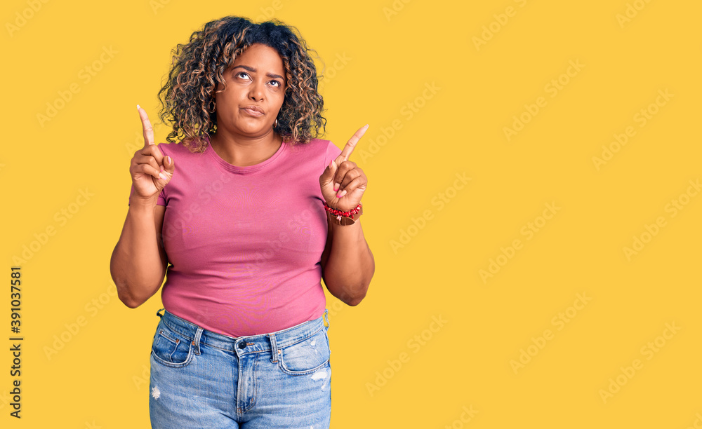 Young african american plus size woman wearing casual clothes pointing up looking sad and upset, indicating direction with fingers, unhappy and depressed. Young african american plus size woman wearing casual clothes pointing up looking sad and upset, indicating direction with fingers, unhappy and depressed.