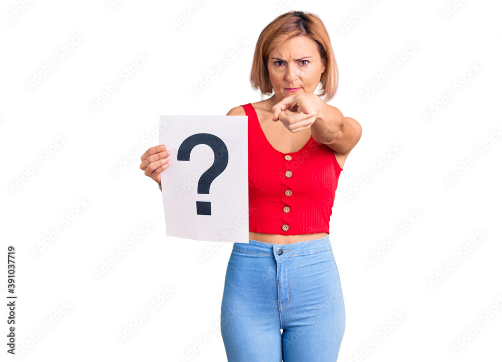 Young blonde woman holding question mark pointing with finger to the camera and to you, confident gesture looking serious Young blonde woman holding question mark pointing with finger to the camera and to you, confident gesture looking serious
