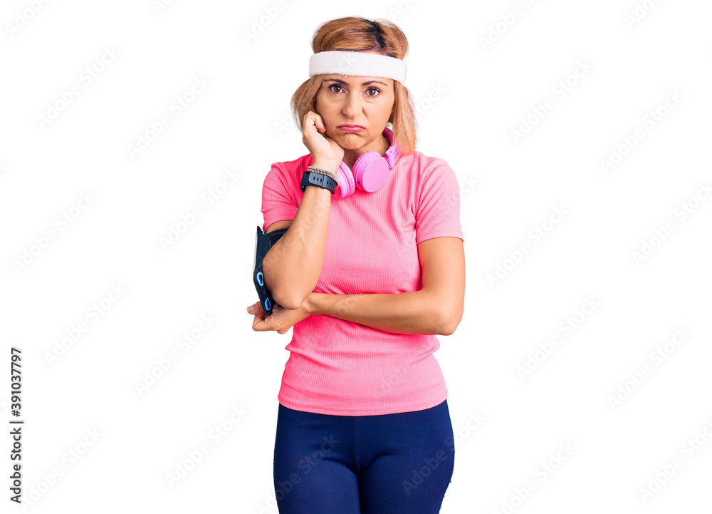 Young blonde woman wearing sportswear and headphones thinking looking tired and bored with depression problems with crossed arms. Young blonde woman wearing sportswear and headphones thinking looking tired and bored with depression problems with crossed arms.