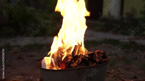 Paper documents and letters burn in fire in the trash bucket. A man throws other papers into the fire, destruction of evidence. All of them burning out.
