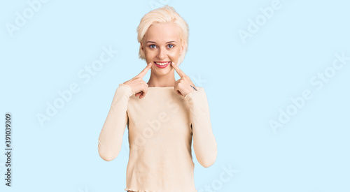 Young blonde woman wearing casual clothes smiling with open mouth  fingers pointing and forcing cheerful smile