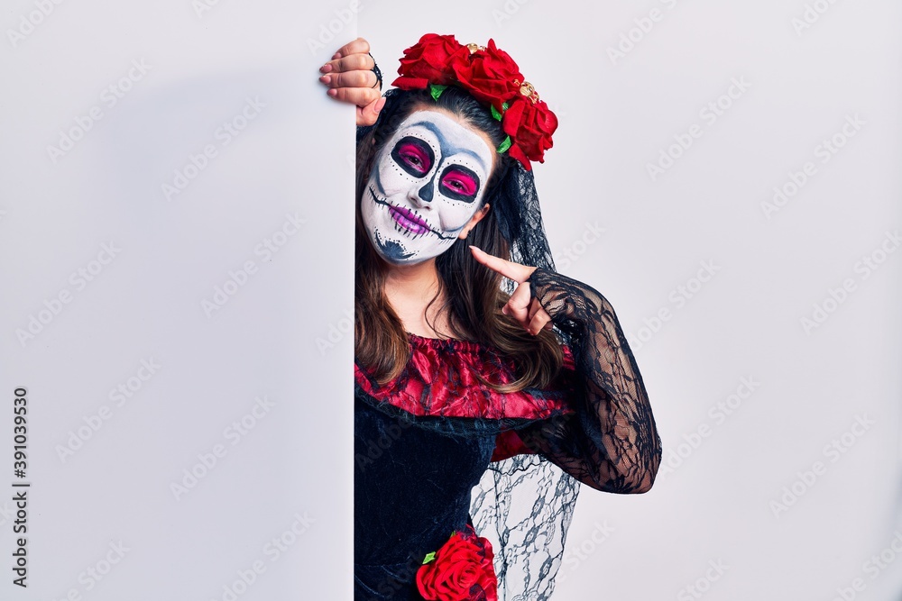 Young woman wearing day of the dead custome holding blank empty banner smiling cheerful showing and pointing with fingers teeth and mouth. dental health concept.