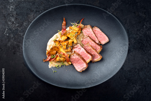 Modern style fried dry aged wagyu roast beef steak with chanterelle and bacon in cream sauce offered as close-up in a design plate