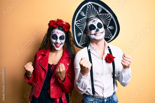 Couple wearing day of the dead costume over yellow very happy and excited doing winner gesture with arms raised  smiling and screaming for success. celebration concept.