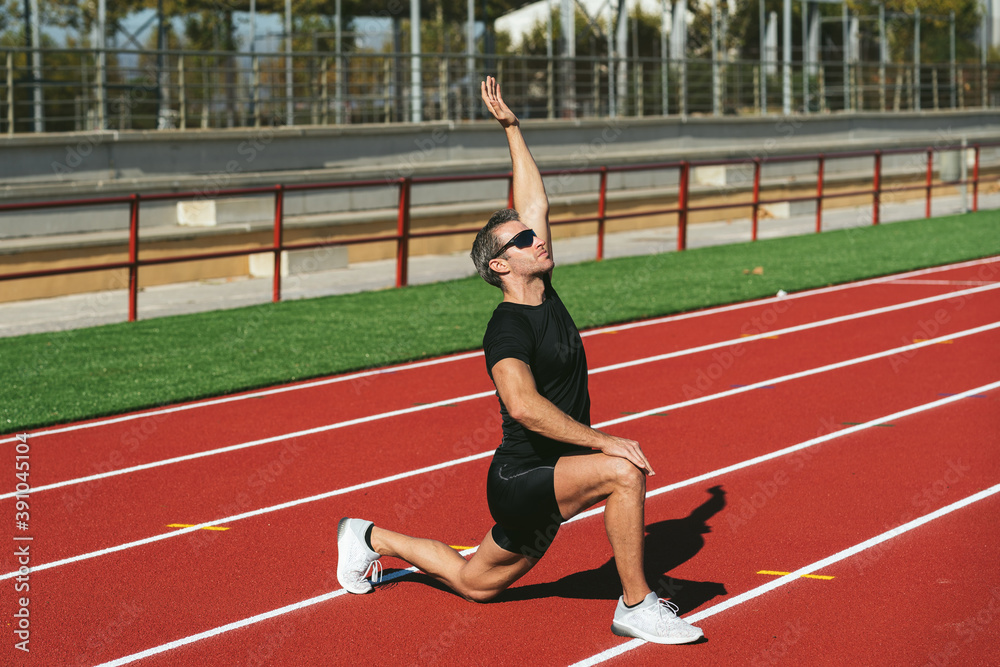 Mature fitness man with glasses stretching on the red running track. Lifestyle and sports