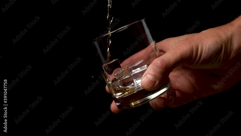 Pouring golden whiskey into a glass with ice cubes. Holding in hand on a black background. Close up. Slow motion Pouring golden whiskey into a glass with ice cubes. Holding in hand on a black background. Close up. Slow motion