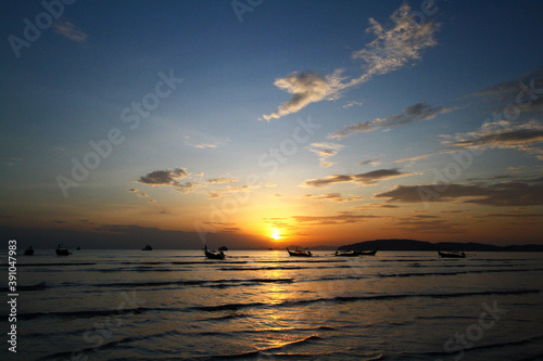 Beautiful silhouette of ship and long tail boat on sea or ocean with blue sky and cloud at sunset, sunrise or twilight time at Krabi, Thailand. Beauty in nature with wave and Transportation concept 
