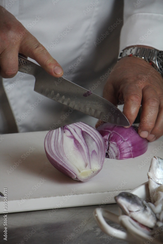 Cuoco taglia cipolla rossa di Tropea su tagliere. Cucina professionale.  Stock Photo