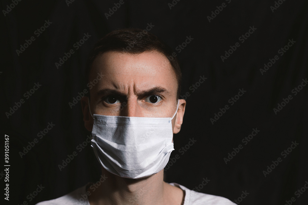 Astonished man in medical mask frowning and looking at camera on black background Astonished man in medical mask frowning and looking at camera on black background