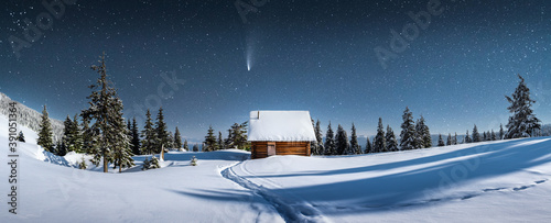 Fantastic winter landscape panorama with wooden house in snowy mountains. Starry sky with Milky Way and snow covered hut. Christmas holiday and winter vacations concept