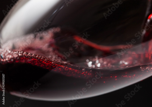 Close up of crystal glass of red wine with bubbles on black.