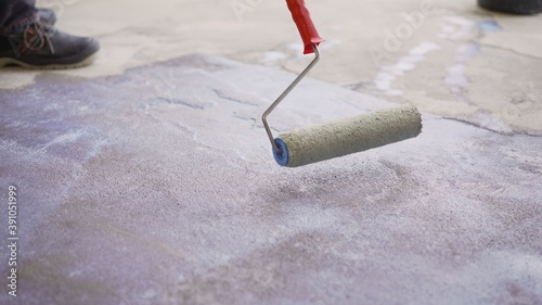 Concrete floor priming is the final preparatory stage for surface strengthening. Priming the concrete floor with a long handle roller. Floor priming process.