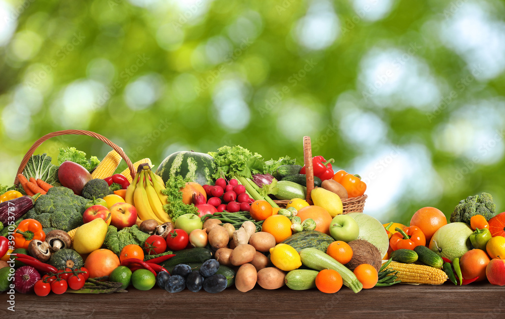 Assortment of fresh organic vegetables and fruits on wooden table against blurred green background Assortment of fresh organic vegetables and fruits on wooden table against blurred green background