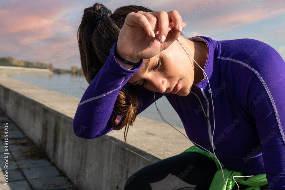 Naklejka premium Young beautiful handsome active fitness woman or girl wipes sweat from her forehead after hard workout training outdoor and taking a break after jogging and running cardio exercise close up