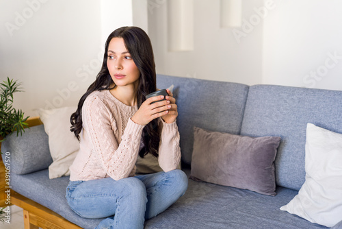 Young woman drinking tea and dreaming sitting on the couch in the bright apartment.