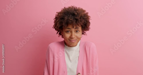 Beautiful curly woman closes eyes and anticipates for something happened holds breath from awaiting then sighs with relief afraids of phobia watches horror film alone poses indoor against rosy wall photo