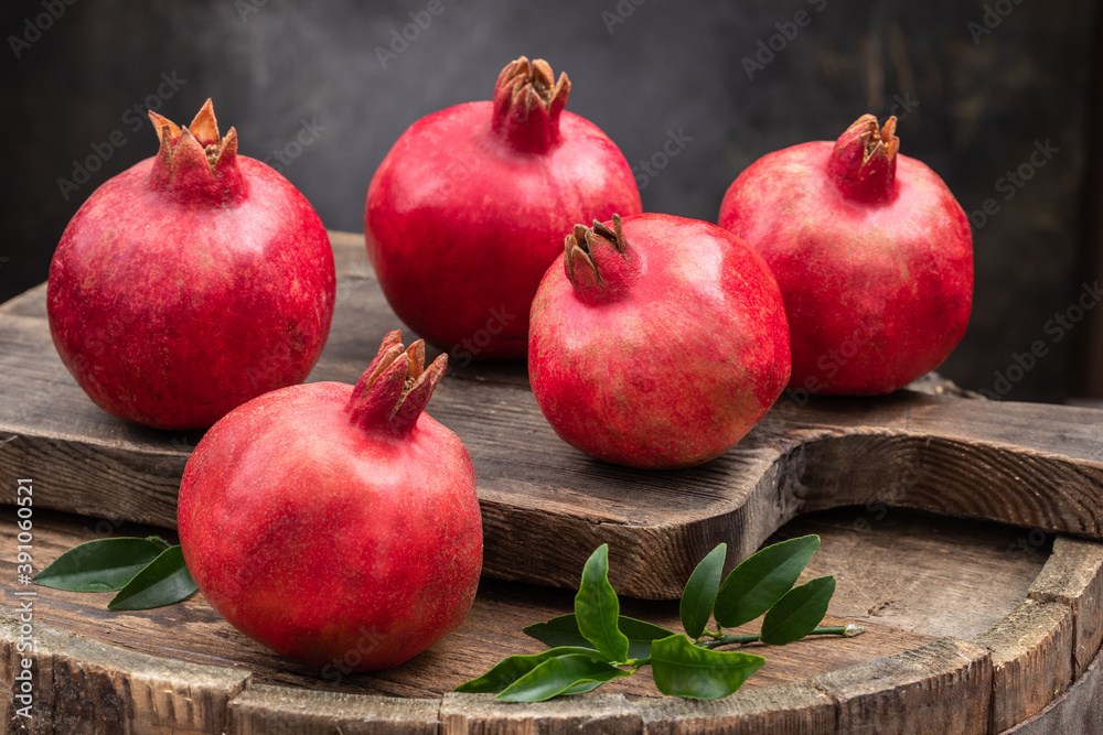 Ripe pomegranate fruits with pomegranate leaves on a wooden old board, side view, dark vintage background. Ripe pomegranate. Ripe pomegranate fruits with pomegranate leaves on a wooden old board, side view, dark vintage background. Ripe pomegranate.