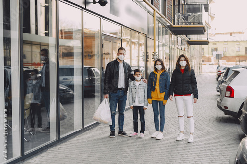 Family in protective masks. People comes out of the supermarket with purchases. Coronavirus theme.