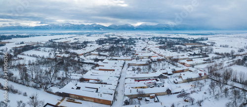 Aerial drone view over a small village located in an open field at the feet of Fagaras Mountains. Winter season and snow and fog is everywhere.