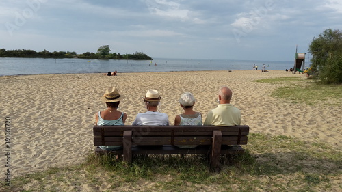Gruppe von älteren Menschen sitzt auf einer Bank am Strand und blickt aufs Wasser