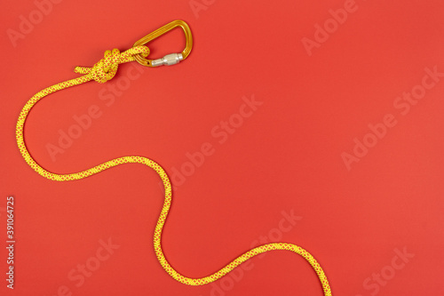 Foto Overhand knot with orange carabiner and yellow climbing rope on red background