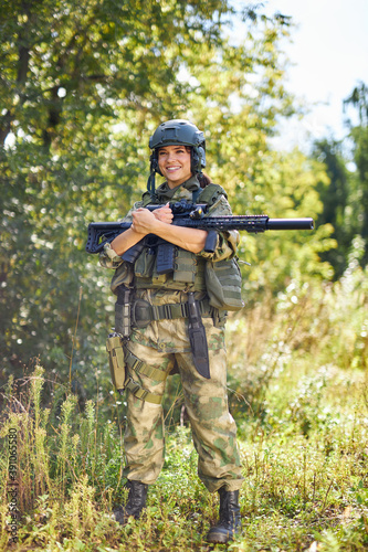 portrait of confident military woman with a gun in forest, hunter female in camouflage suit with a gun stand in nature alone