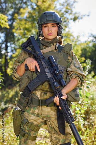 portrait of confident military woman with a gun in forest, hunter female in camouflage suit with a gun stand in nature alone