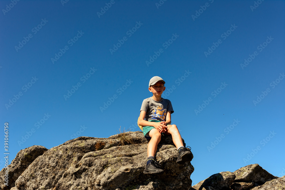 boy sitting on the edge of a large rocky rock, summer hike in the mountains, the top of the mountain.