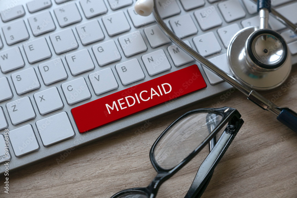 Selective focus of stethoscope, glasses and computer keyboard with red key written with Medicaid on a wooden background. Selective focus of stethoscope, glasses and computer keyboard with red key written with Medicaid on a wooden background.