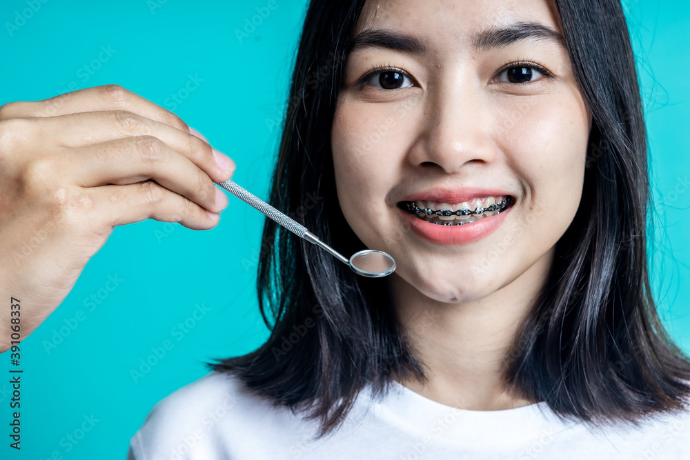 Asian woman wearing dental braces pointing to tooth sample and smiling with her healthy white teeth isolated shot on blue background Asian woman wearing dental braces pointing to tooth sample and smiling with her healthy white teeth isolated shot on blue background