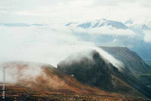 Atmospheric alpine landscape to giant low cloud above rocky mountains. Big thick clouds above highland valley. Wonderful scenery on high altitude. View from slope on snowy mountain range with glacier.