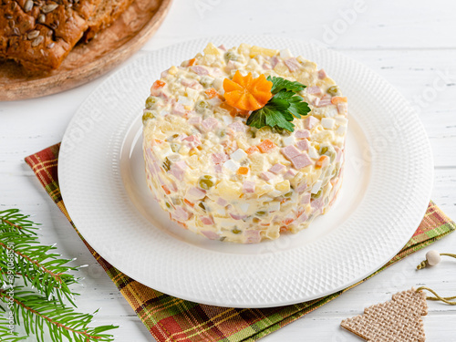 Olivier salad. Traditional russian dish for celebrating new year and christmas. White wooden table background. Festive table setting. Fir tree branches, bread, wooden fir tree. Close up view.