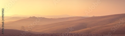 Morning pink colored panorama of Tuscany landscape with mist, rolling hills and farm houses