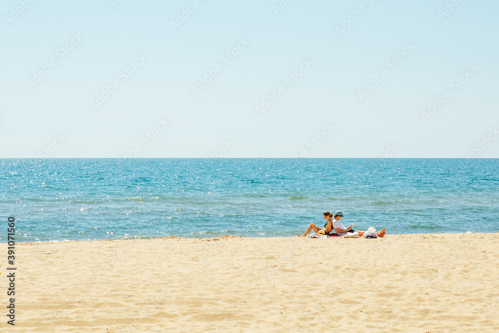 Gribovka, Ukraine - July 2, 2020: couple sitting on the beach reading book. sunbathing Gribovka, Ukraine - July 2, 2020: couple sitting on the beach reading book. sunbathing
