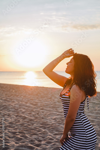 young beautiful sexy woman in dress walking bay sandy beach at sunset