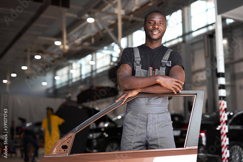 portrait of positive afro american auto mechanic in uniform posing after work, he is keen on repairing cars, automobiles.