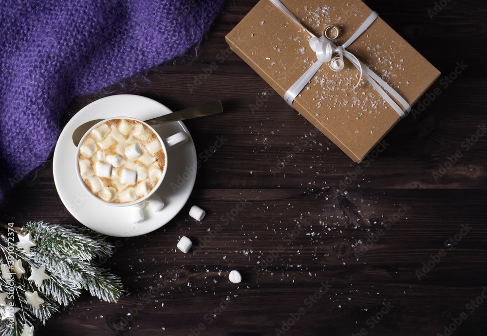 This photo shows a cup with hot cocoa and marshmallows, a knitted blanket, a gift box and fir branches on a dark wooden background with snow. Horizontal orientation, copy space, flat lay. This photo shows a cup with hot cocoa and marshmallows, a knitted blanket, a gift box and fir branches on a dark wooden background with snow. Horizontal orientation, copy space, flat lay.