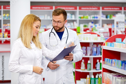 team of young caucasian chemists or druggists discussing medicines, check medical indications, in white medical gowns, at work place