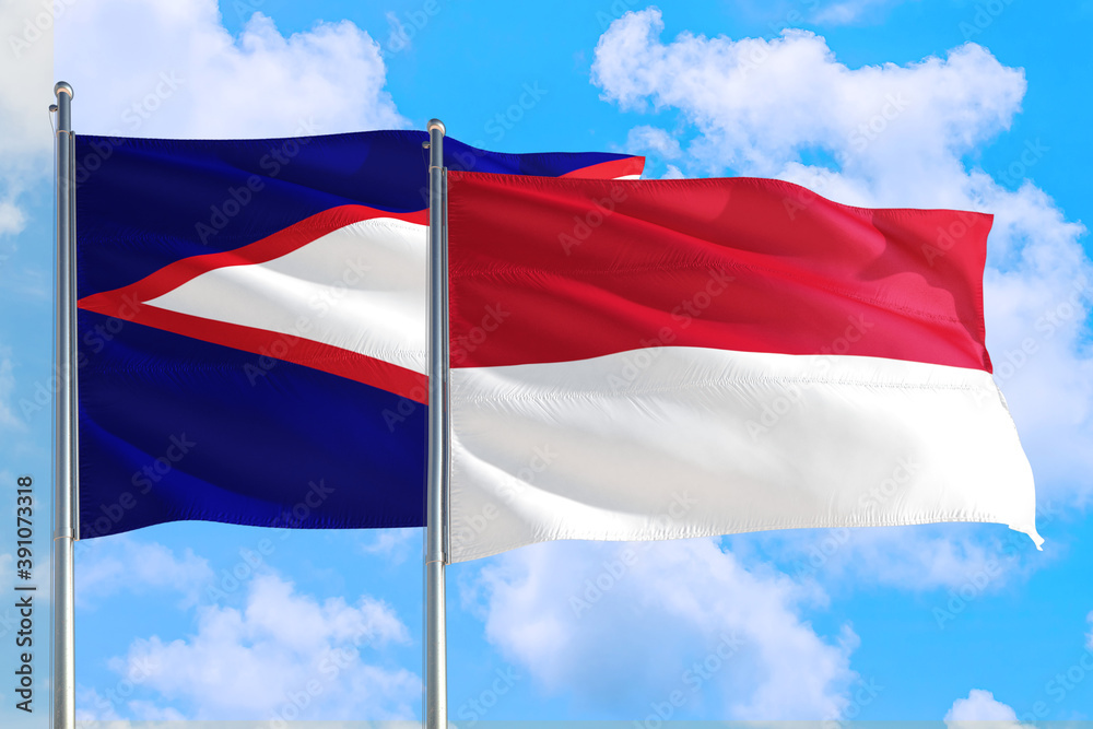 Naklejka premium Monaco and American Samoa national flag waving in the windy deep blue sky. Diplomacy and international relations concept.
