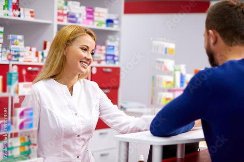 caucasian friendly pharmacist has a nice conversation with a client, helps to find a medication, ask about symptoms and what is he suffering from
