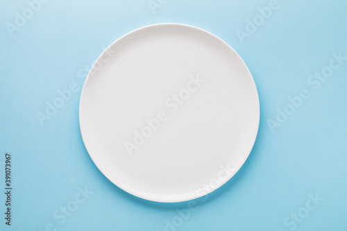 Empty white ceramic plate on a blue background, top view. Food background