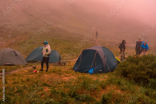 Tourists and tents near the lake, fog in the mountains near the lake, rain clouds in the Carpathians, a tent camp near the lake, Lake Brebeneskul.