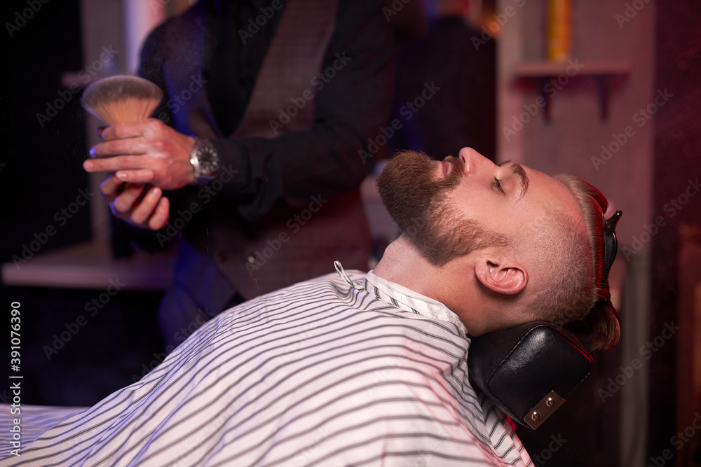 Fototapeta premium modern barber male begins to cut hair of client, making stylish beard, hair cut in salon, use brush