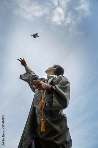 Low angle view of male high school graduate tossing his graduation cap up into the sky