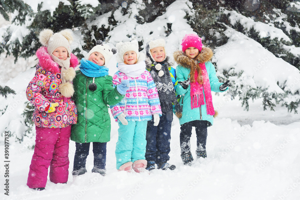 a group of children in colorful bright winter clothes smile against the background of the winter forest and snow. Winter fashion, warm clothes, winter entertainment, Christmas holidays.