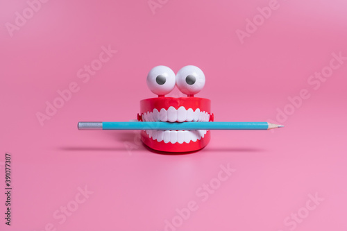 A plastic toy in the form of red jaws with white teeth and eyes holds a pencil between its teeth. Copywriting concept photo