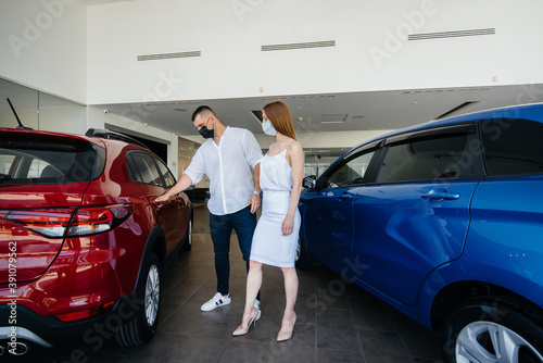 Young couple in masks selects a new vehicle and consult with a representative of the dealership in the period of the pandemic. Car sales, and life during the pandemic © Andrii
