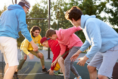 group of young male teenagers in colourful hoodies playing basketball outdoors in the street
