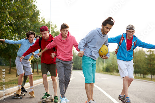 modern friendly guys in casual clothes skateboarding and showing exciting tricks, in the park, city life. extreme sport concept