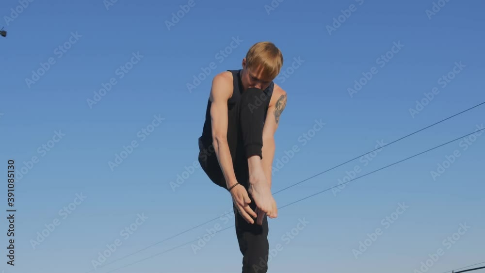 Caucasian man with a tattoo on his shoulder doing yoga on the roof. He stands on one leg and raises the other leg, and tilts the body towards the leg. Balance and balance concept Caucasian man with a tattoo on his shoulder doing yoga on the roof. He stands on one leg and raises the other leg, and tilts the body towards the leg. Balance and balance concept